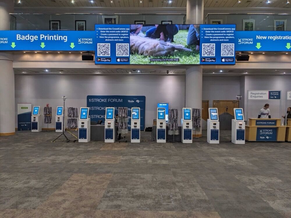 A row of branded Max kiosks under badge printing signage at the UK Stroke Forum